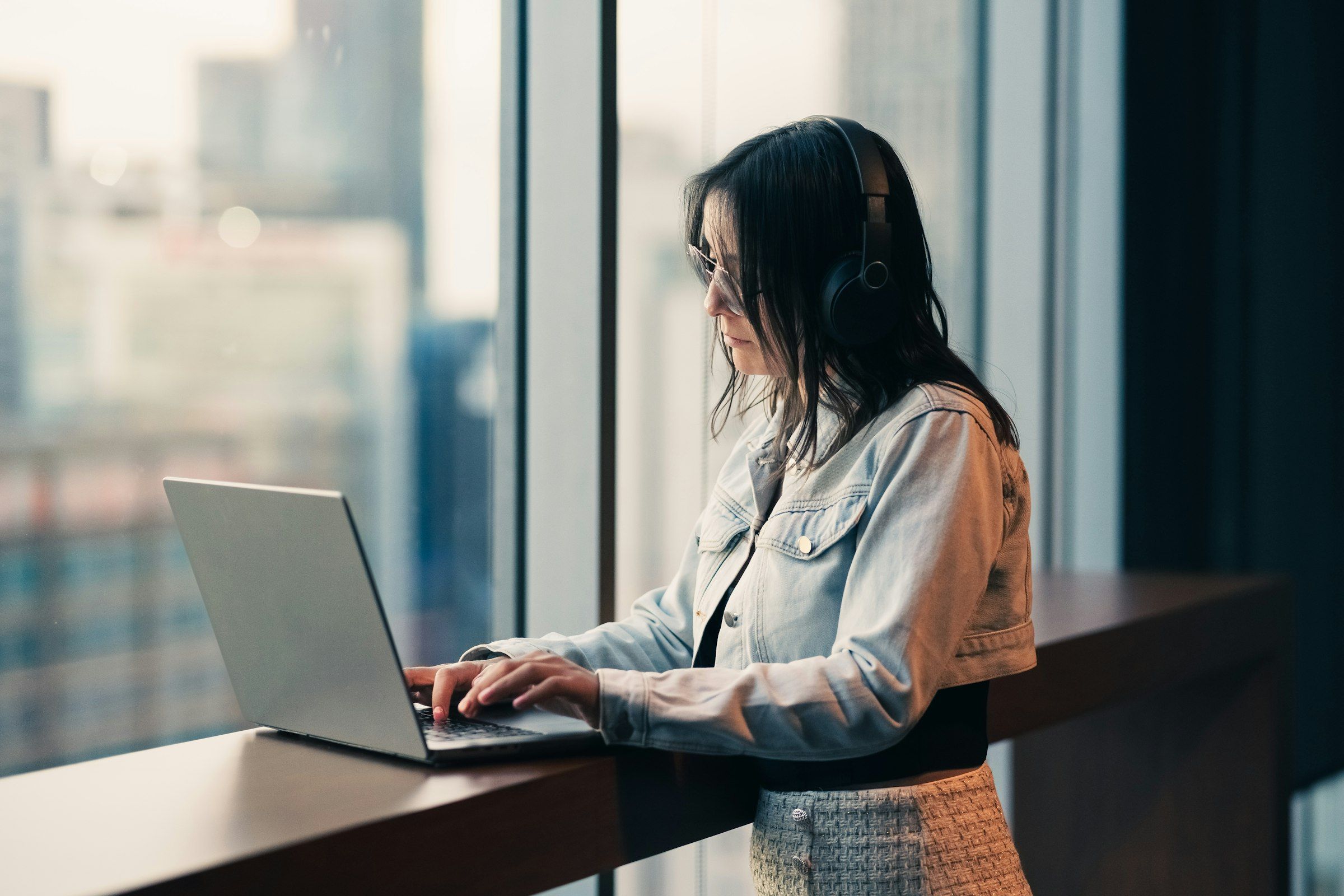 Professional working on a laptop beside a window overlooking the city